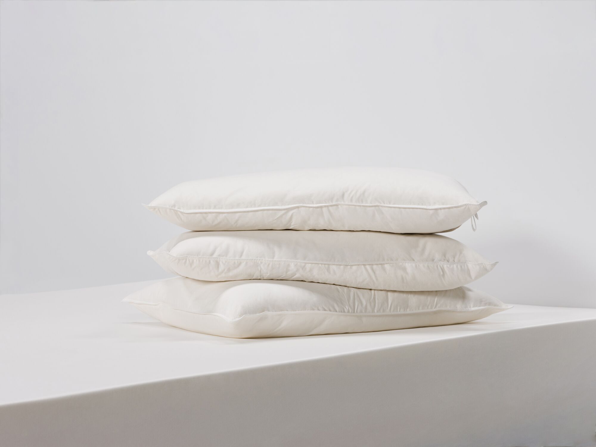 Three queen size feather pillows stacked side view